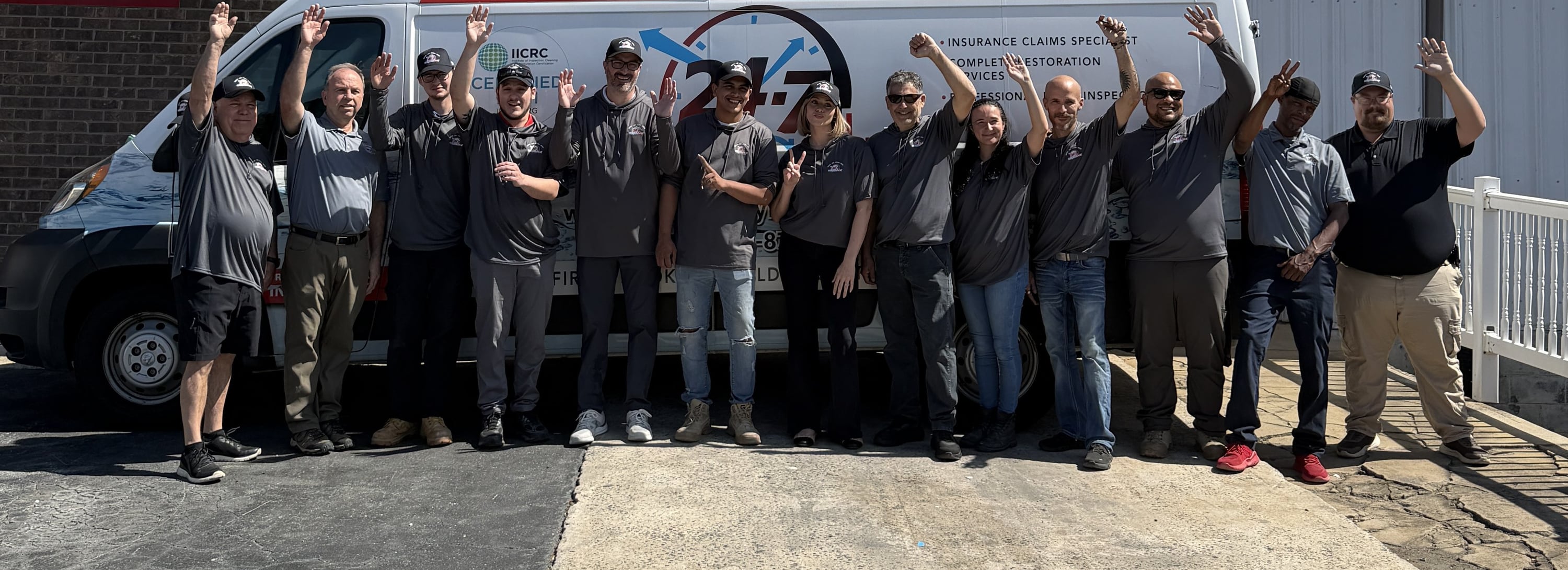 The 24-7 AquaDry crew, arms raised in front of a wrapped response van outside the shop